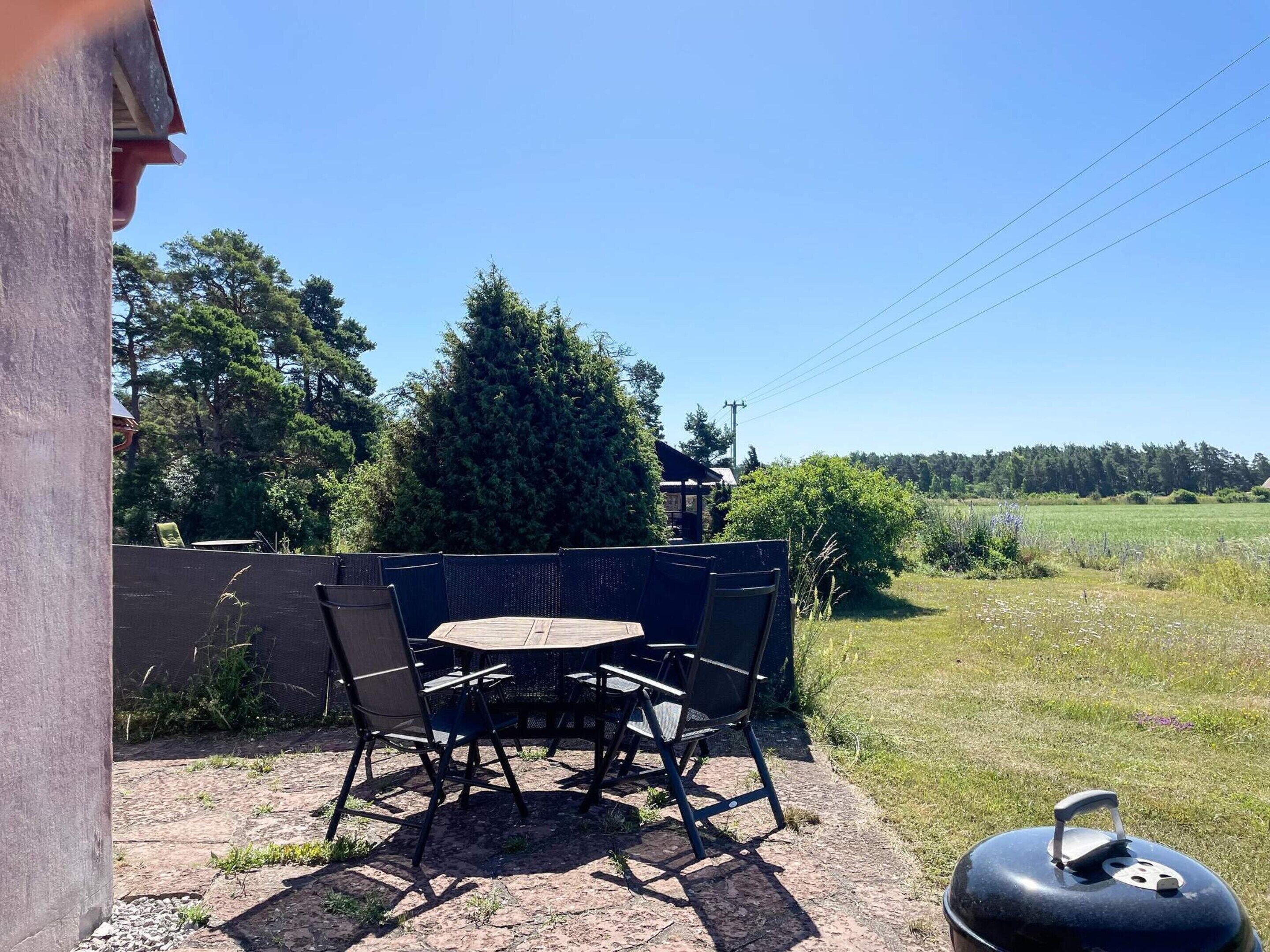 An outdoor patio with a table and chairs, a grill, and a view of a field and trees.