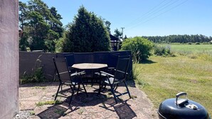 An outdoor patio with a table and chairs, a grill, and a view of a field and trees.
