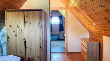A room with a sloped ceiling, wooden walls, a bed, a dresser, and a fan.