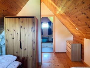 A room with a sloped ceiling, wooden walls, a bed, a dresser, and a fan.