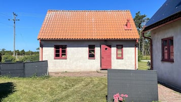A two-story house with a red-tiled roof, a red door, and a small garden area with a potted plant.