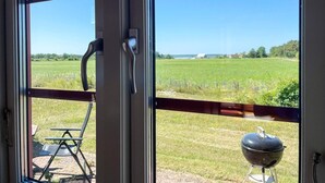 A window with a view of a grassy field and a barbecue grill outside.