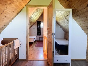 A bedroom with a sloped ceiling, a wooden door, a bed, and a small bedside table.