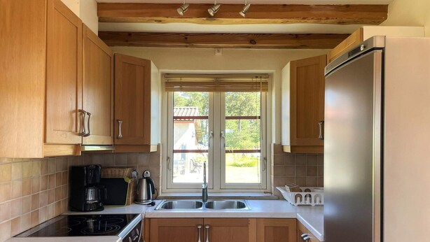 A kitchen with wooden cabinets, a stainless steel refrigerator, a built-in oven, and a window with blinds.