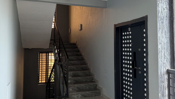 Eine Treppe führt zu einer Zwischenebene mit einer Tür, auf der '18' steht, und einer Überwachungskamera an der Decke.