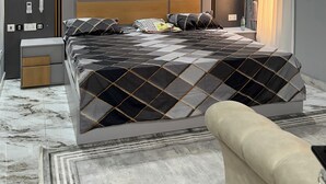 Ein modernes Schlafzimmer mit einem großen Bett, einem Nachttisch, einer Lampe und einem Fenster mit Vorhängen.