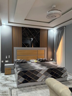 Ein modernes Schlafzimmer mit einem großen Bett, einem Nachttisch, einer Lampe und einem Fenster mit Vorhängen.