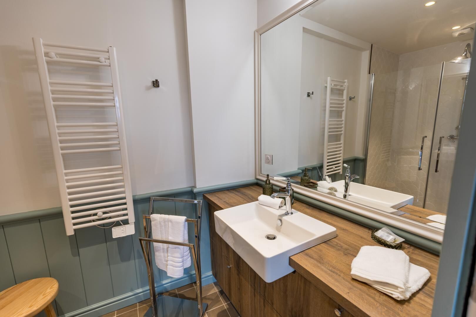 Un baño con un lavabo blanco, un espejo grande, un perchero para toallas y una zona de ducha.