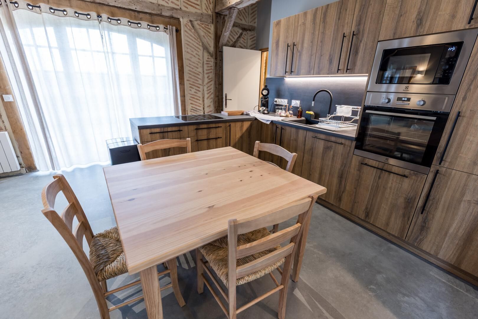 Une cuisine moderne avec des meubles en bois, un four encastré et un coin repas comprenant une table et des chaises en bois.