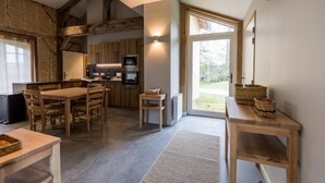 Une cuisine moderne avec des poutres en bois, un coin repas avec une table et des chaises, et une grande fenêtre offrant une vue sur l’extérieur.