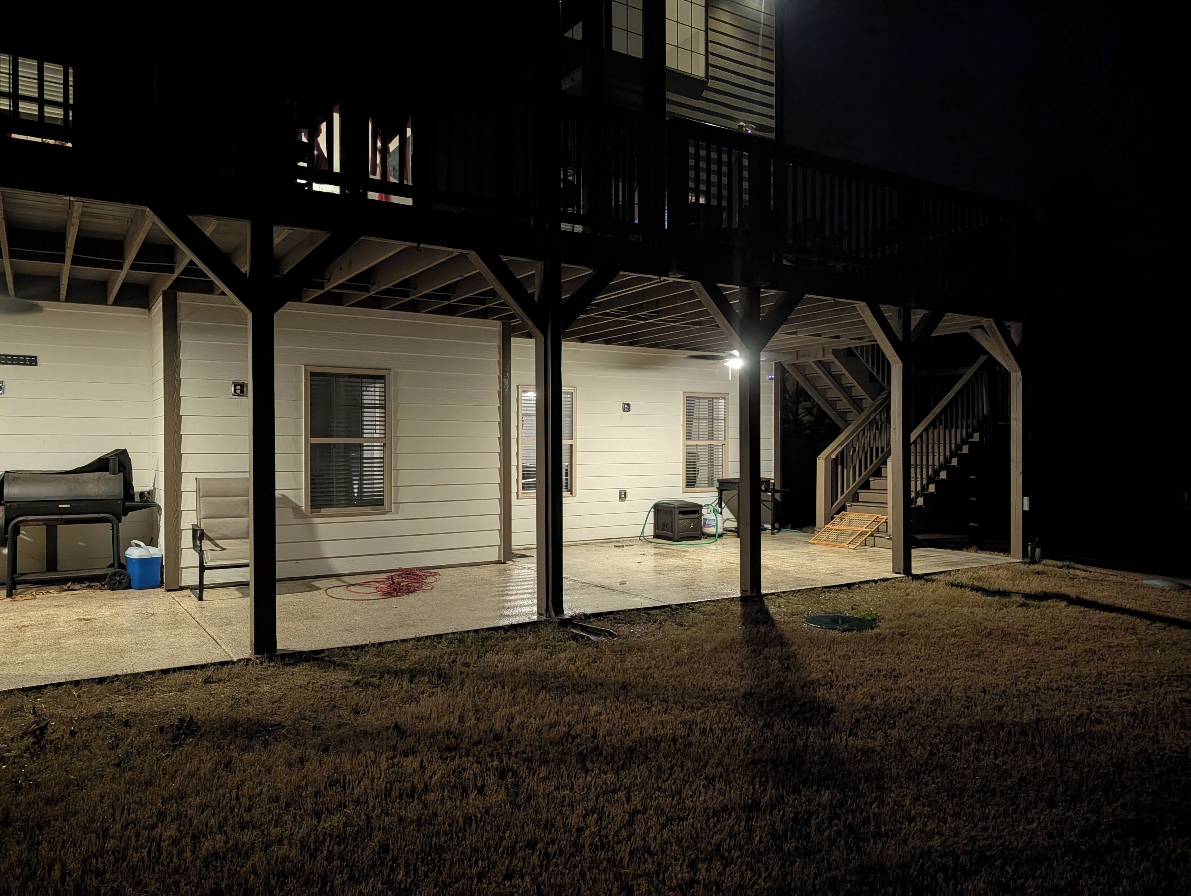 A covered outdoor area with a grill, a hose, and a ladder.