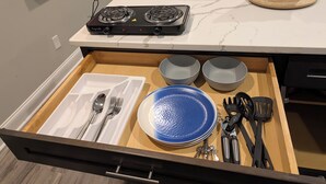 A kitchen with a stove, two bowls, a plate, and utensils in a drawer.