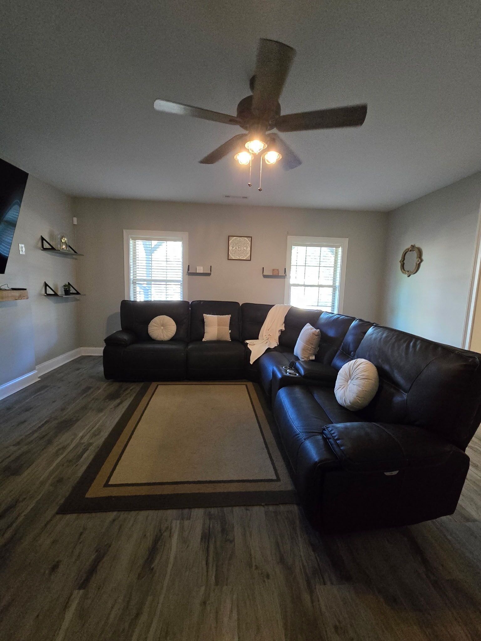 A living room with a sectional sofa, a ceiling fan, and a large window.
