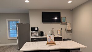 A modern kitchen with a marble island, bar stools, a refrigerator, a microwave, and a coffee maker.