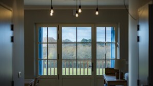 Ein Zimmer mit großem Fenster, einer Tür, einem Tisch und Pendelleuchten.