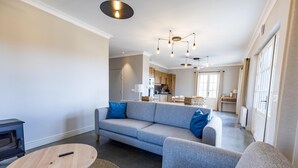Ein modernes Wohnzimmer mit einem grauen Sofa, einem runden Holztisch und einer Küche im Hintergrund.