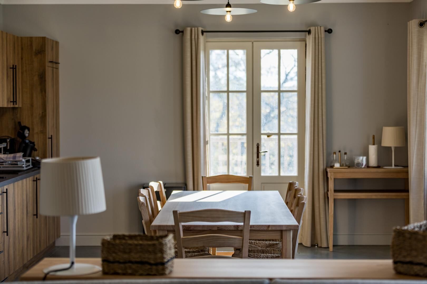Een eetruimte met een tafel, stoelen, een lamp en een raam met gordijnen.
