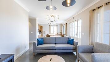 Een moderne woonkamer met een grijze bank, een ronde salontafel en hanglampen.