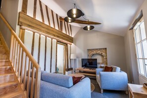 Ein modernes Interieur mit einer Holztreppe, einem Kamin und einer Sitzecke mit zwei Sesseln und einem Sofa.