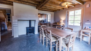 Un interior rústico con una mesa y sillas de madera, una chimenea y una zona de cocina.