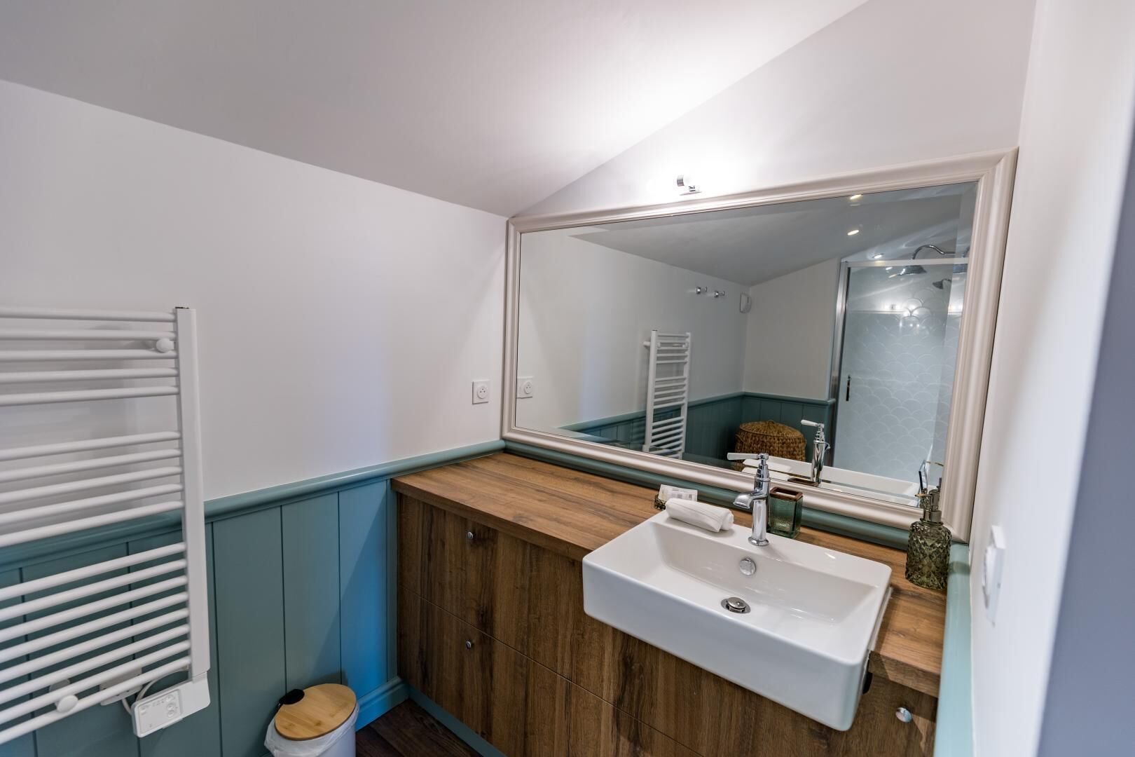 Une salle de bain avec un lavabo blanc, un meuble-lavabo en bois, un porte-serviettes et un miroir.