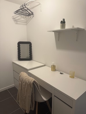 A white desk with a chair, a towel, a mirror, a lamp, and a hanging rack.