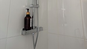 A shower with a handheld showerhead, a wall-mounted control, and a soap dispenser.