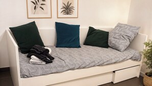 A white sofa with a patterned cover, multiple pillows, a small plant, and a woven rug.