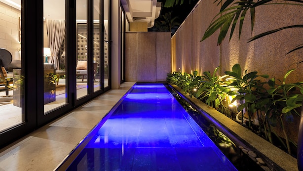 Una fuente interior estrecha con una piscina iluminada en azul, rodeada de plantas en macetas y un diseño de interiores moderno.