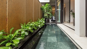 Una estrecha fuente con plantas a un lado, una entrada de puertas de cristal y una pared blanca al otro.