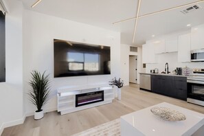 Een moderne woonkamer met een flatscreentelevisie, een open haard en een keuken met donkere kasten en roestvrijstalen apparatuur.