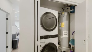 A compact laundry room with two washing machines and a large water heater. - The Neon Circuit Loft (Phoenix)