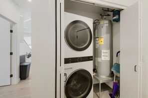 A compact laundry room with two washing machines and a large water heater. - The Neon Circuit Loft (Phoenix)