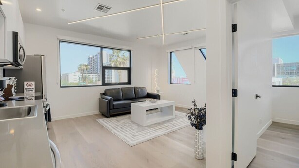 A modern living room with a sofa, coffee table, and a view of the city through large windows. - The Neon Circuit Loft (Phoenix)