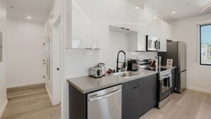 A modern kitchen with white cabinets, stainless steel appliances, and a large window. - The Neon Circuit Loft (Phoenix)