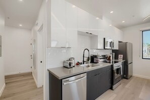 A modern kitchen with white cabinets, stainless steel appliances, and a large window. - The Neon Circuit Loft (Phoenix)