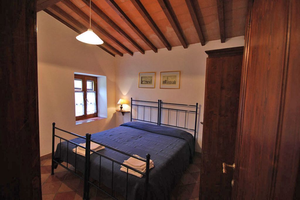 A bedroom with a bed, a window, a door, and a wall-mounted lamp.