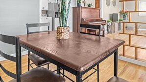 Uma sala de jantar com mesa e cadeiras de madeira, um piano e uma cozinha ao fundo.