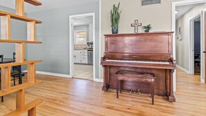Um quarto espaçoso com piso de madeira, um piano de cauda, uma estante de madeira e um vaso de plantas.