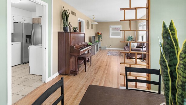 Uma sala de estar ampla com um piano, uma mesa de jantar com cadeiras, um sofá e uma planta.