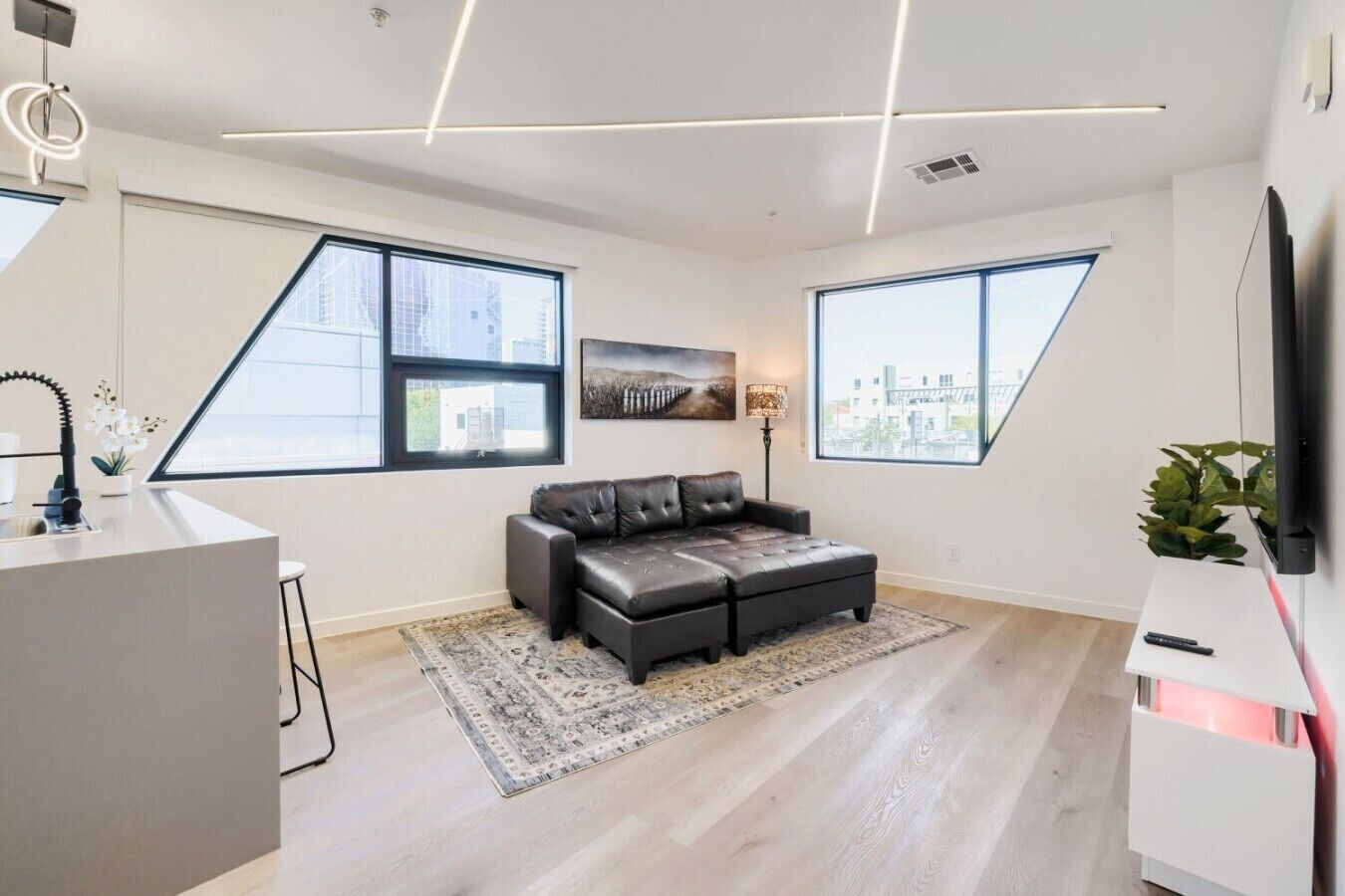 Una sala moderna con un sofá, un televisor de pantalla plana y ventanas grandes.