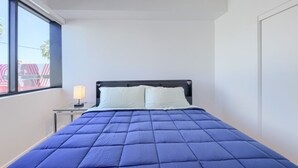 A bedroom with a bed, a nightstand, a lamp, and a window. - Phoenix Rustic Urban Retreat (Phoenix)
