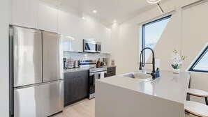 A modern kitchen with stainless steel appliances, a central island, and a window providing natural light. - Phoenix Rustic Urban Retreat (Phoenix)