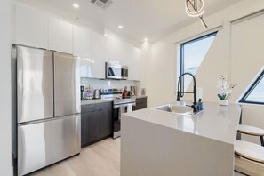 A modern kitchen with stainless steel appliances, a central island, and a window providing natural light. - Phoenix Rustic Urban Retreat (Phoenix)