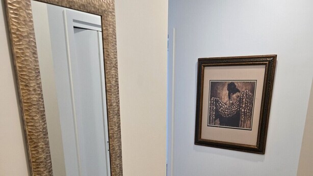 Un couloir avec un miroir et une œuvre d’art encadrée accrochée au mur.