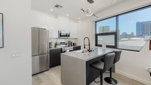 Une cuisine moderne dotée d’un îlot central, d’appareils électroménagers en acier inoxydable et d’une grande fenêtre offrant une vue sur la ville.