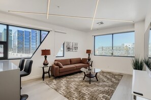 Ein modernes Wohnzimmer mit Sofa, Couchtisch und Sesseln, großen Fenstern mit Blick auf die Stadt und einem gemusterten Teppich.