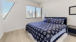 Une chambre à coucher avec un lit, un ventilateur de plafond, une fenêtre et une vue sur les bâtiments environnants.