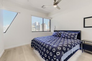 Ein Schlafzimmer mit Bett, Deckenventilator, Fenster und Blick auf Gebäude.