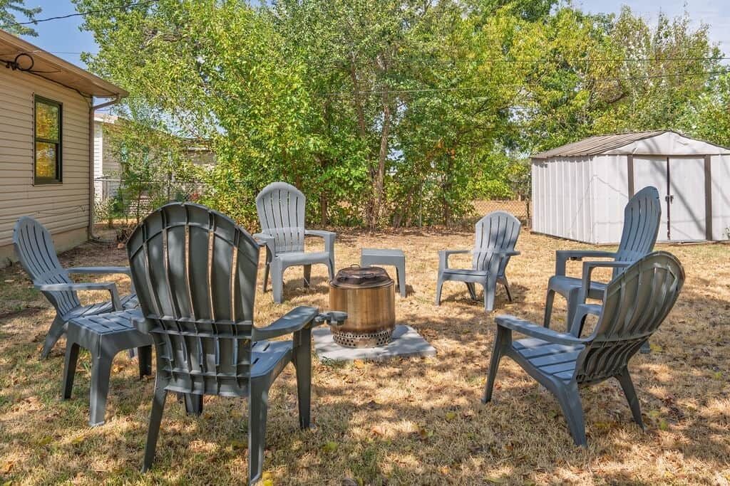 A backyard with Adirondack chairs arranged around a central fire pit, a shed, and a house in the background.